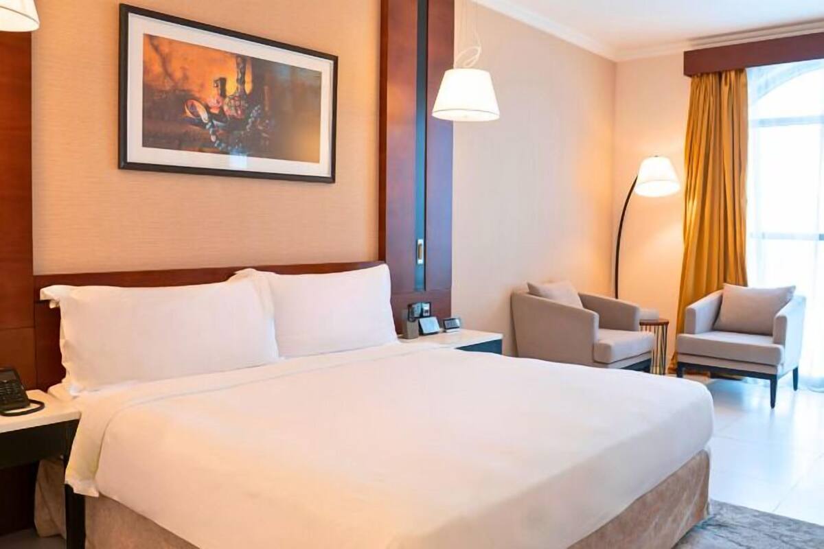 A hotel room with a large bed, a desk with a phone, a chair, and a lamp.