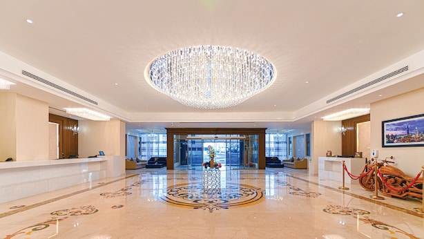 A spacious lobby with a large chandelier, a reception desk, and a decorative floor pattern. -  Asma Hotel (Dubai)