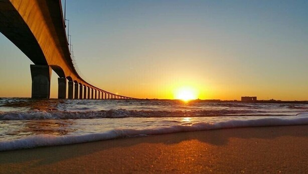 Tramonto sulla costa con un ponte sull'acqua.