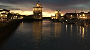 Una veduta sul lungomare con una torre storica e una struttura fortificata, circondata da acque calme e imbarcazioni.