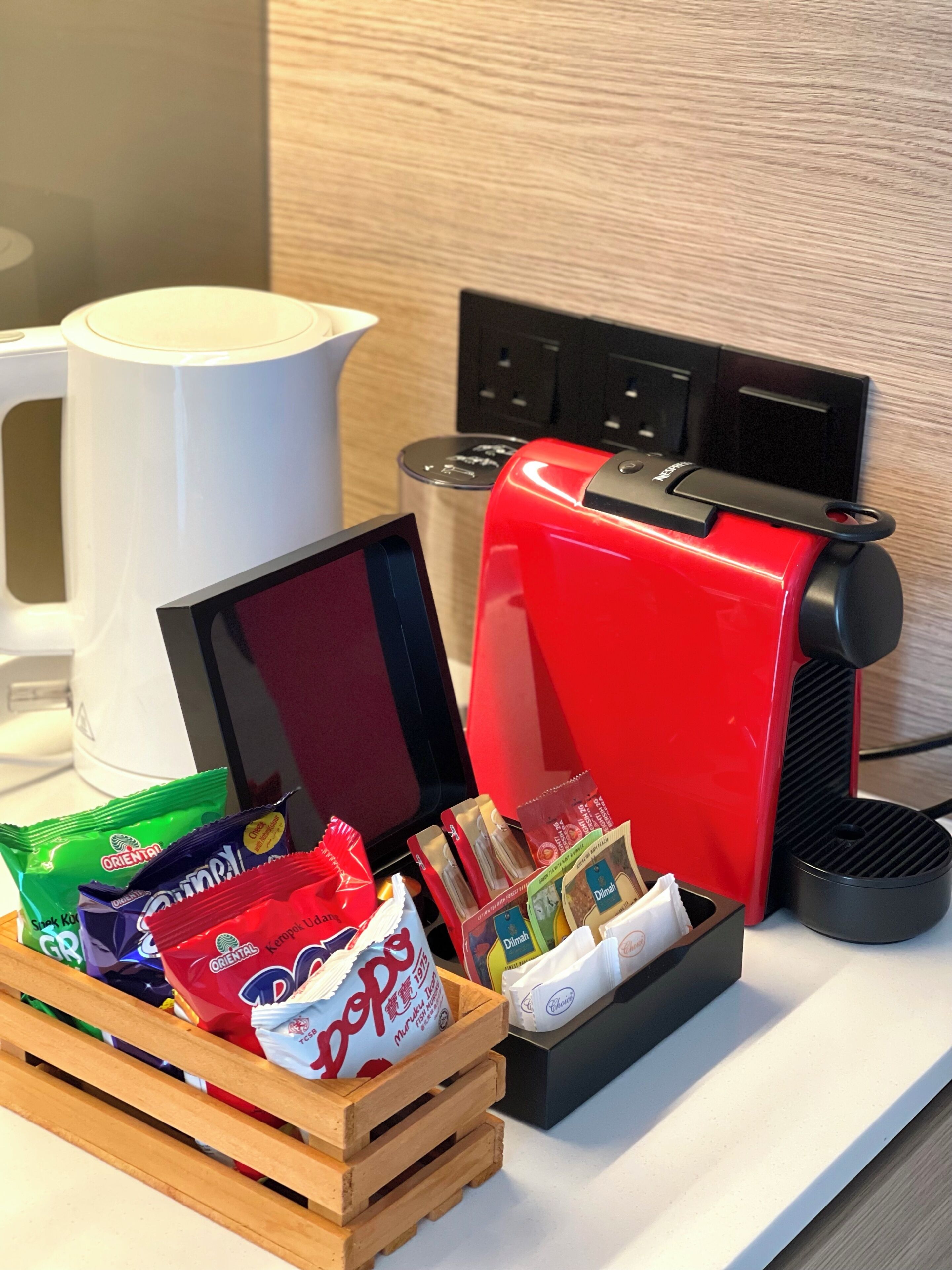 A coffee machine, a white coffee pot, and a wooden crate with snack packets.