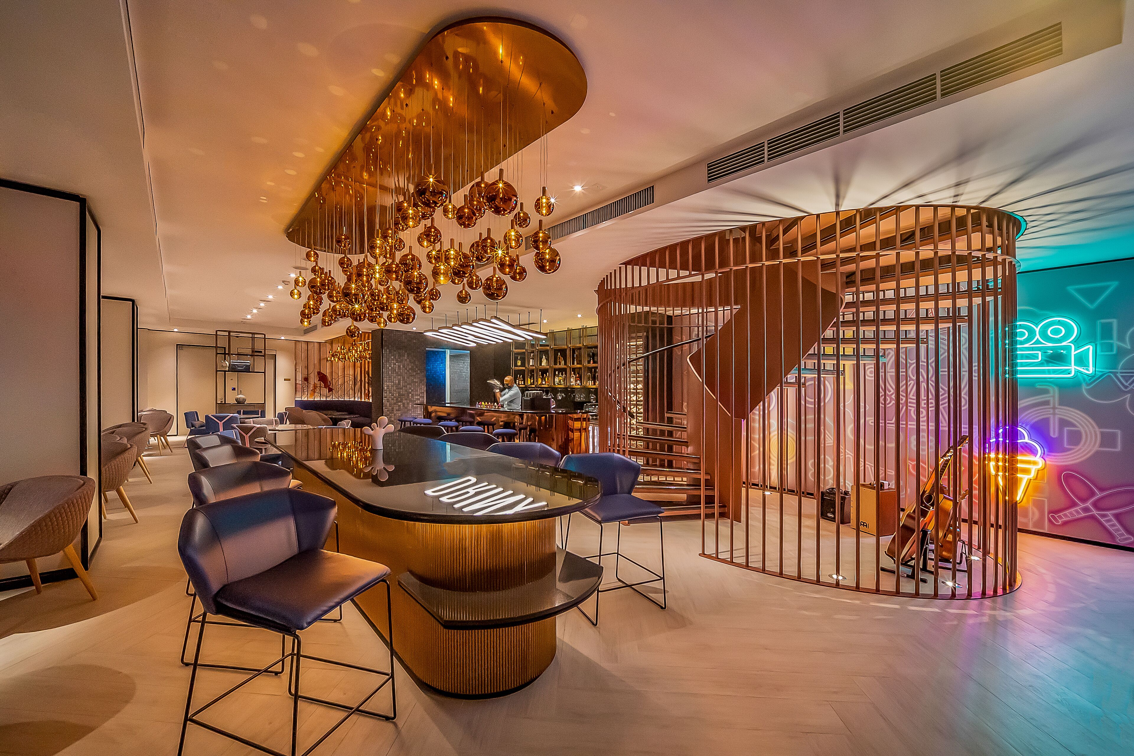 A modern bar area with a curved bar, seating, and a unique ceiling light fixture.