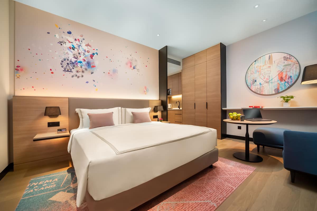 A modern hotel room with a large bed, a desk, and a seating area.