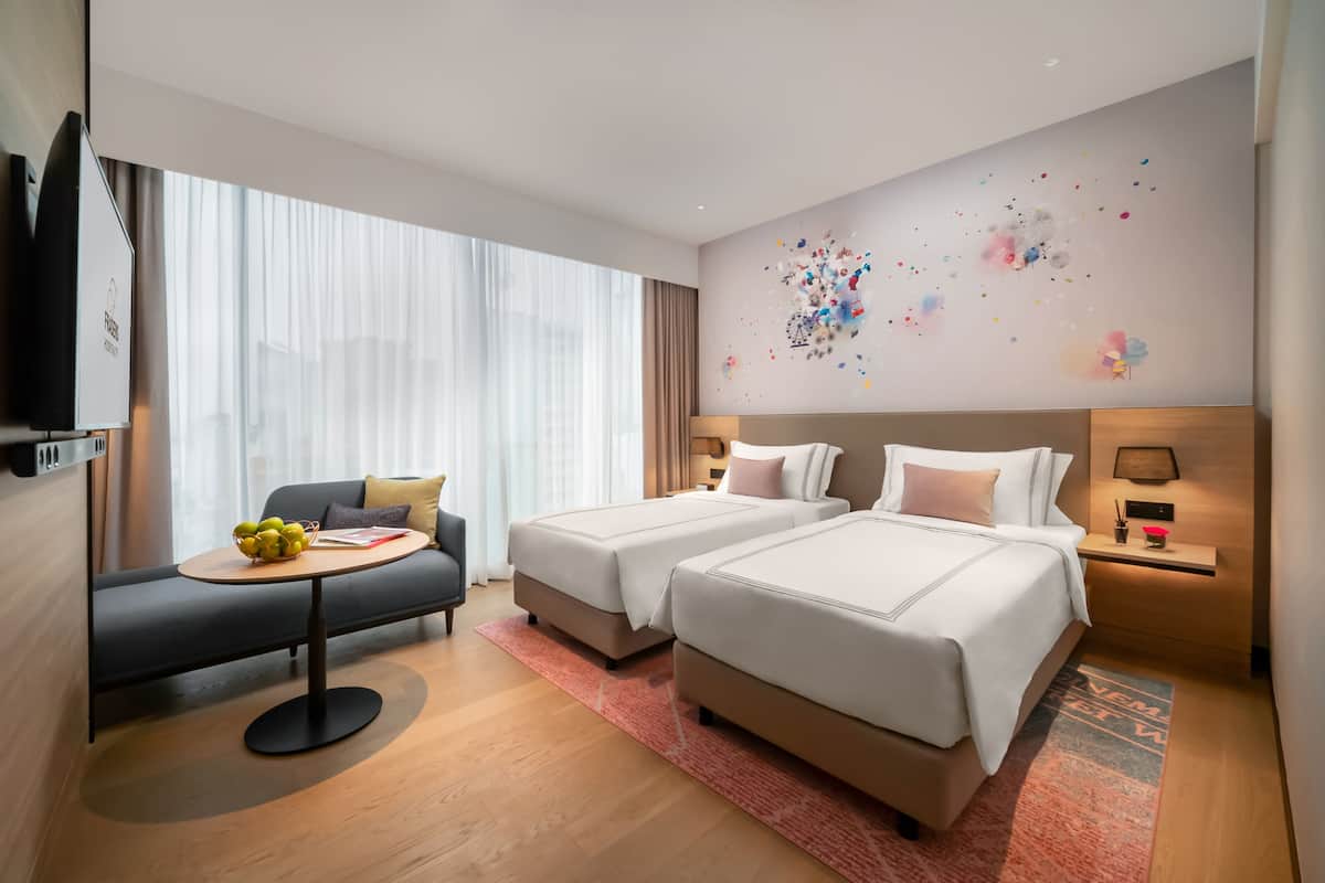 A modern hotel room with two beds, a sofa, a TV, and a large window with sheer curtains.