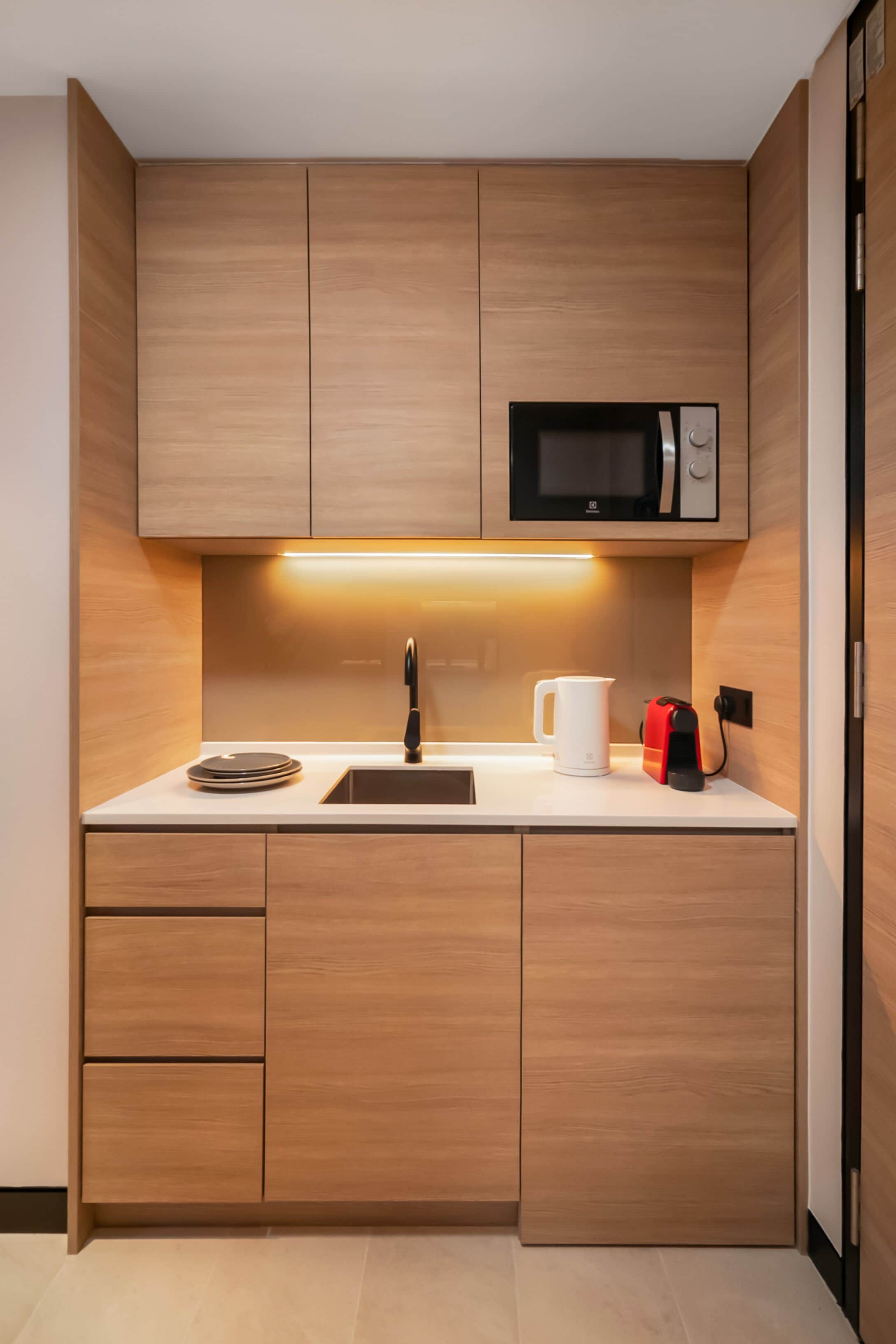 Een moderne keuken met houten kastjes, een zwarte magnetron, een spoelbak en een waterkoker.