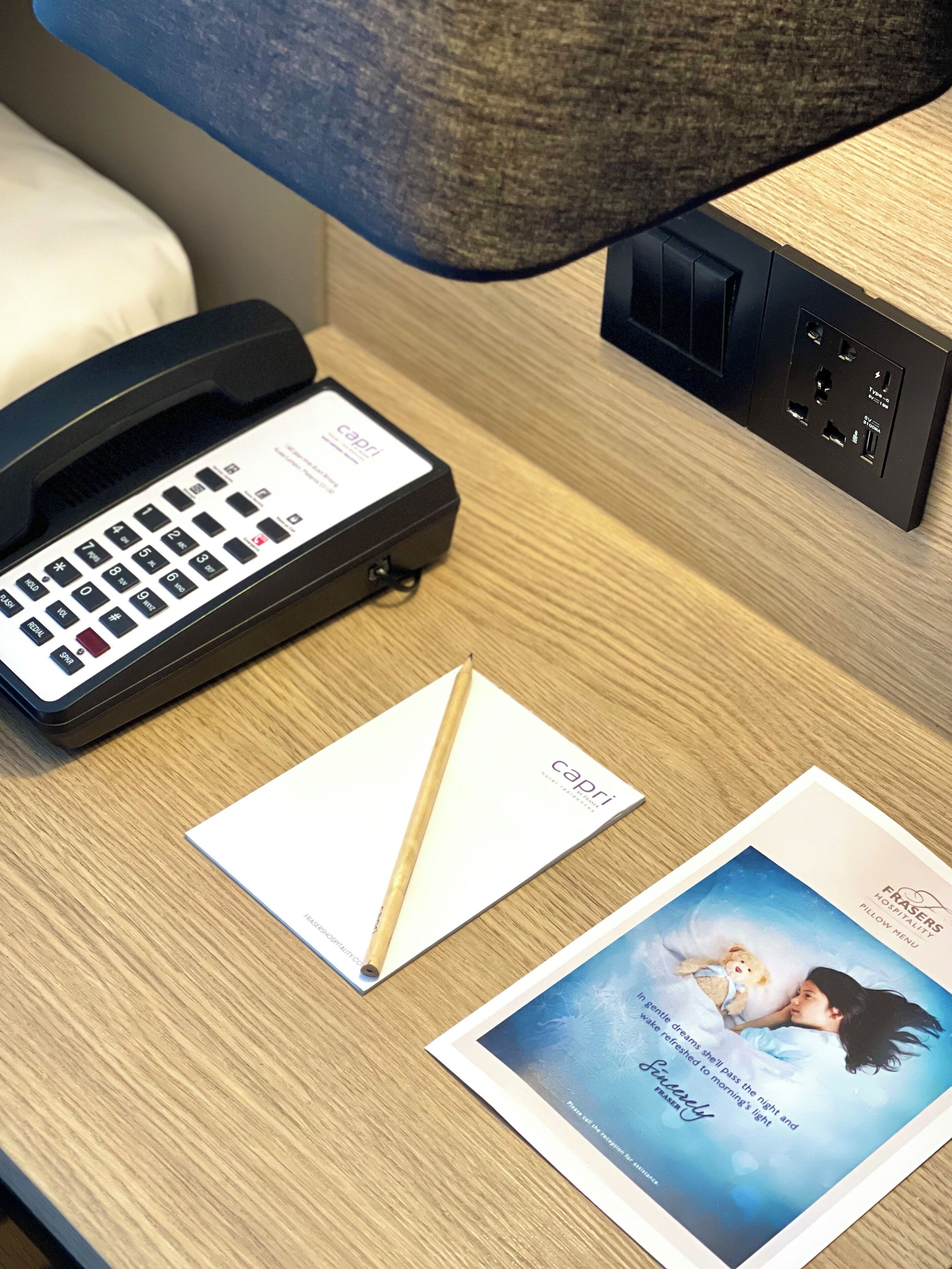 A hotel room with a desk, a telephone, a notepad, and a brochure.