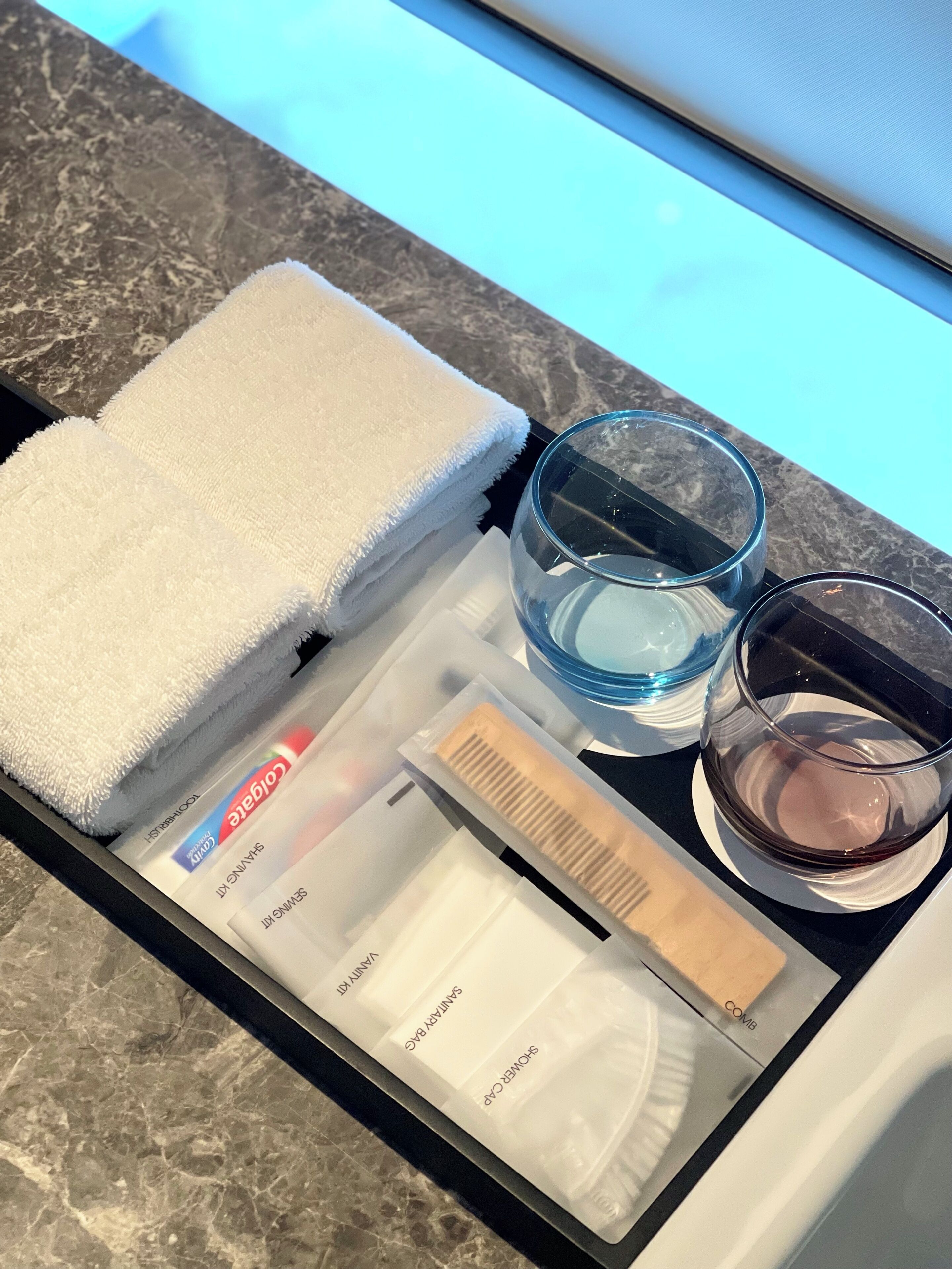 A neatly arranged bathroom with a marble countertop, a white towel, a glass of water, a glass of wine, and toiletries.
