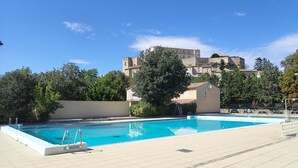 A swimming pool with a ladder, surrounded by a tiled deck, with buildings and trees in the background. - Grignan Provencal Tower – Stunning Views & Elegant Stay (Grignan)