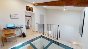 A modern room with a glass staircase, a wooden desk with a laptop, and a bed in the background. - Grignan Provencal Tower – Stunning Views & Elegant Stay (Grignan)