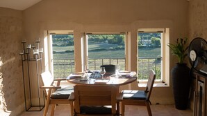 A dining area with a table and chairs, a fan, and a view of vineyards through large windows. - Grignan Provencal Tower – Stunning Views & Elegant Stay (Grignan)