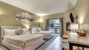 A hotel room with two beds, a dining area, a fireplace, and a balcony with a view of the mountains.