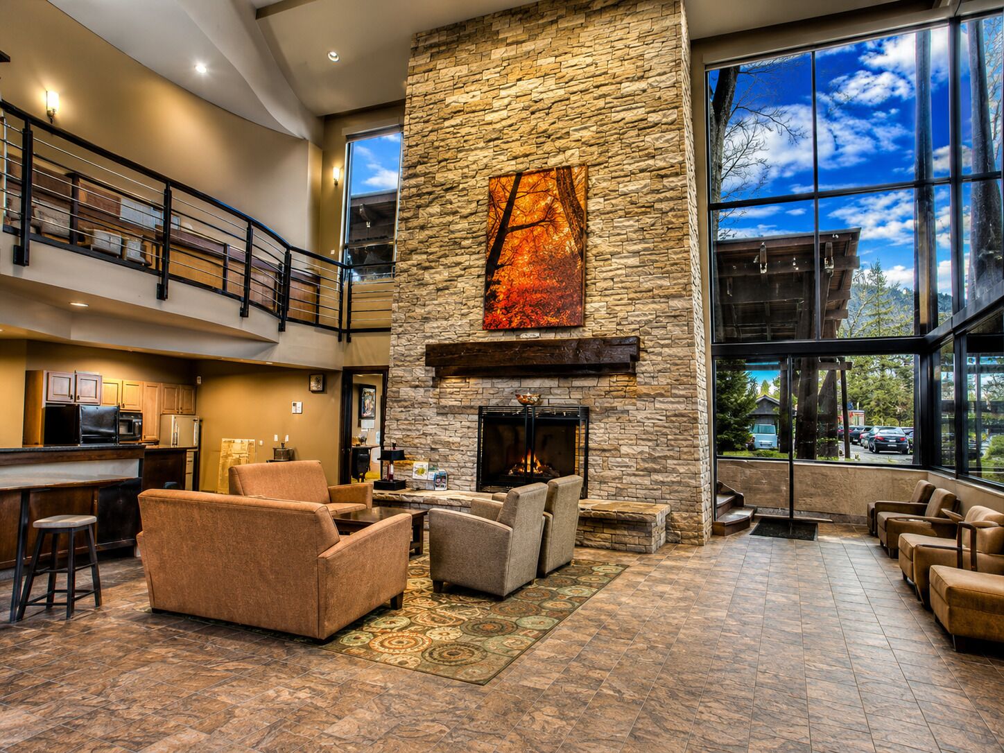 Un vestíbulo amplio con chimenea de piedra, asientos cómodos, zona de cocina y ventanas grandes con vistas al exterior.