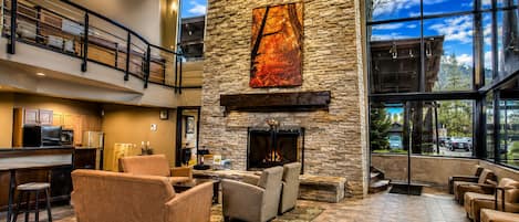Un vestíbulo amplio con chimenea de piedra, asientos cómodos, zona de cocina y ventanas grandes con vistas al exterior.