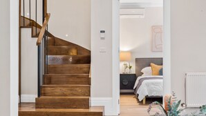 Una escalera de madera que conduce a un dormitorio con cama, mesita de noche, lámpara y radiador.