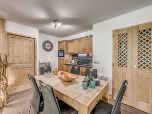 A modern kitchen with wooden cabinets, a microwave, and a sink. There is a dining table with chairs and a fruit bowl.