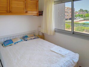 Een slaapkamer met een bed, houten kasten, en een raam met uitzicht op gebouwen en groen.