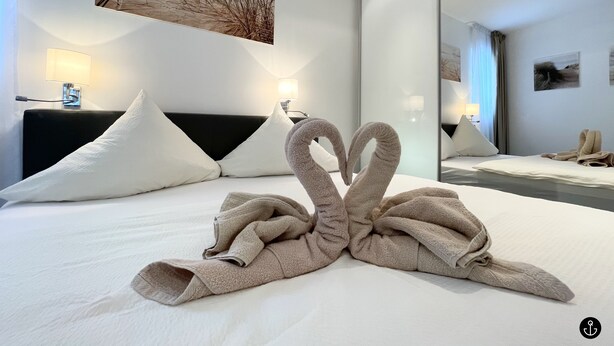 Ein Hotelzimmer mit einem ordentlich bezogenen Bett, zwei Nachttischlampen, einem großen Spiegel und einem Gemälde an der Wand.