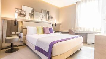 A modern hotel room with a large bed, bedside tables, a desk, and a large window.