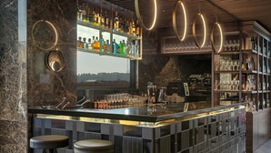 Un bar moderno con mostrador de mármol, taburetes y una variedad de botellas y vasos.