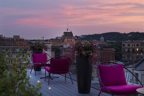 A rooftop terrace with two pink chairs and a large planter with flowers, overlooking a cityscape with historic buildings. - Orazio Palace Hotel (Rome)