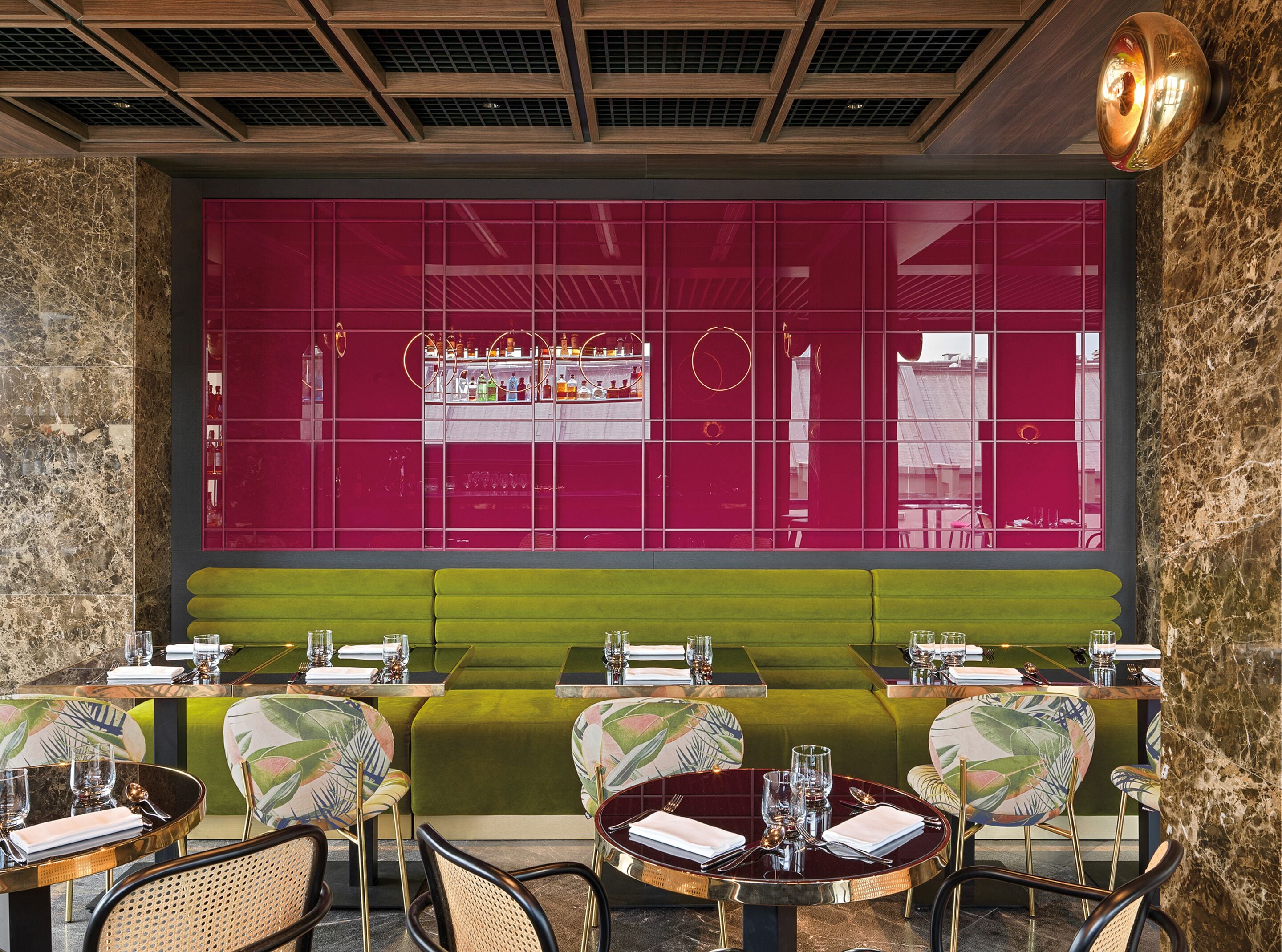 Ein Restaurant mit modernem Interieur, das grüne Polsterbänke, Marmorwände und eine rote Trennwand mit Barbereich zeigt.