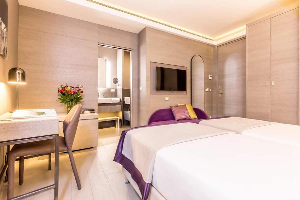 A modern hotel room with a bed, a desk, a chair, a TV, and a wardrobe.