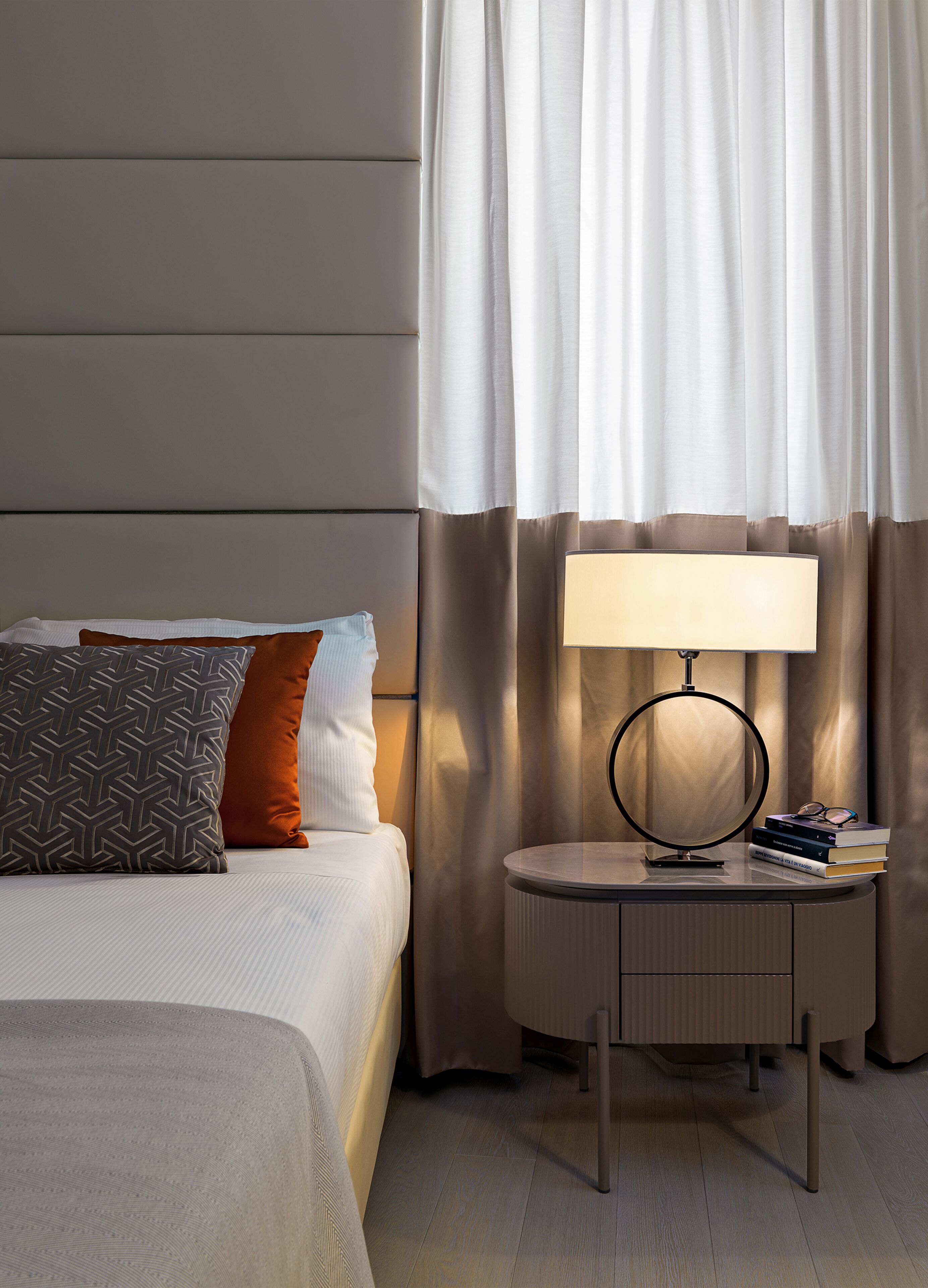 A hotel room with a bed, a bedside table with a lamp, and a curtain.