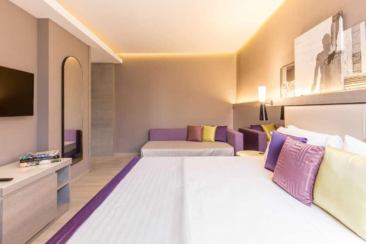 A hotel room with two beds, a TV, a desk, and a mirror.