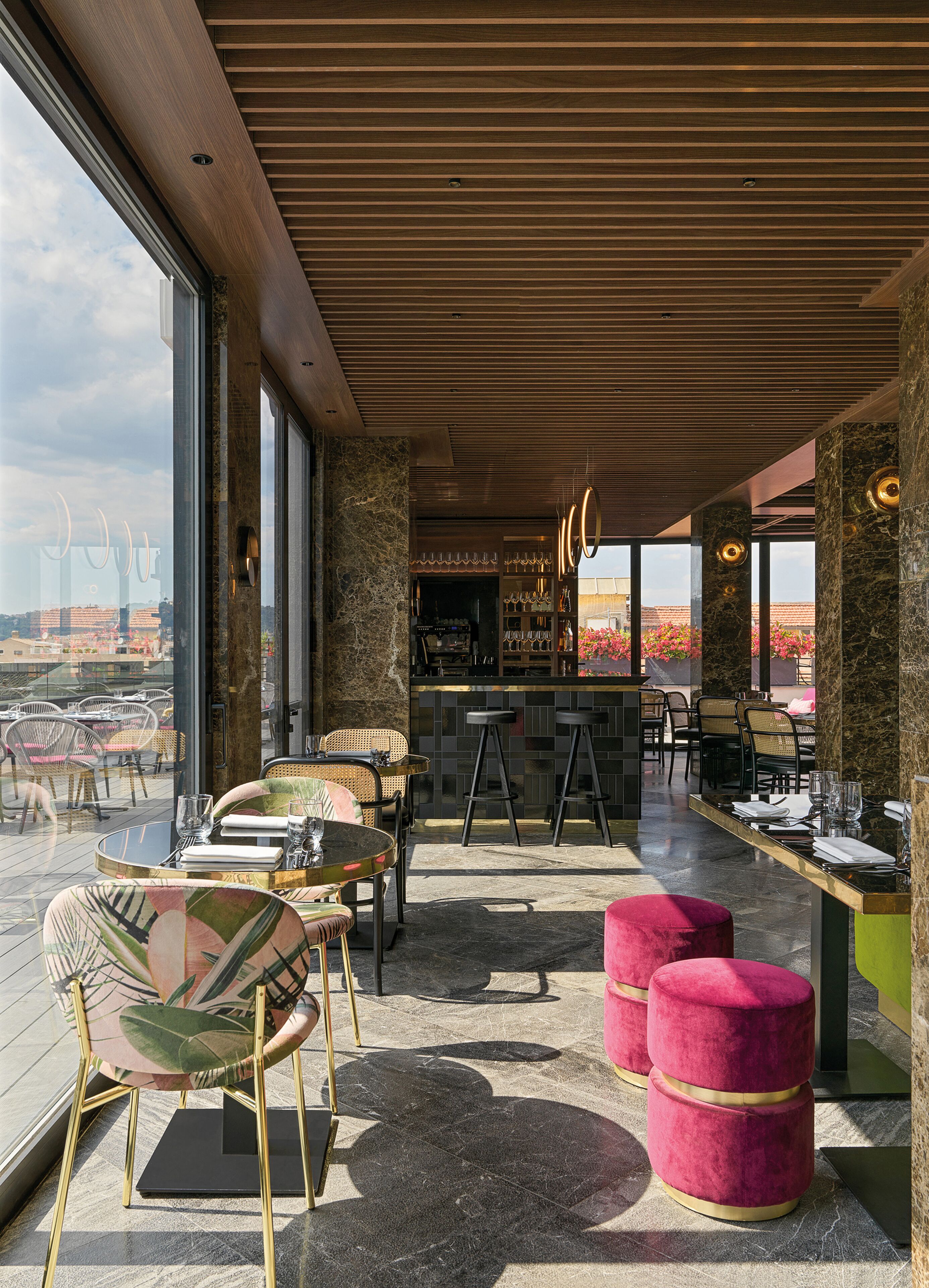 A modern bar area with a wooden ceiling, large windows, and a view of the cityscape.