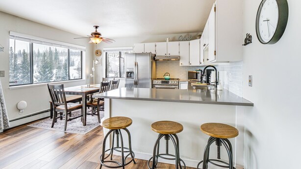 Una cocina moderna con una isla grande, taburetes de bar y vistas al bosque por la ventana.
