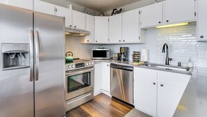 Una cocina moderna con electrodomésticos de acero inoxidable, armarios blancos y un salpicadero de azulejos.