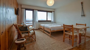 Ein gemütliches Zimmer mit einem Bett, zwei Holzstühlen, einem kleinen Tisch und einem großen Fenster mit Vorhängen.