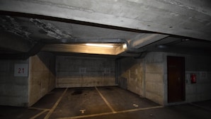 Eine schlecht beleuchtete Tiefgarage mit Betonwänden und nummerierten Stellplätzen.