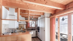 A modern kitchen with wooden beams, white cabinets, and a large window with curtains. - Chalet Mouettes (Riddes)