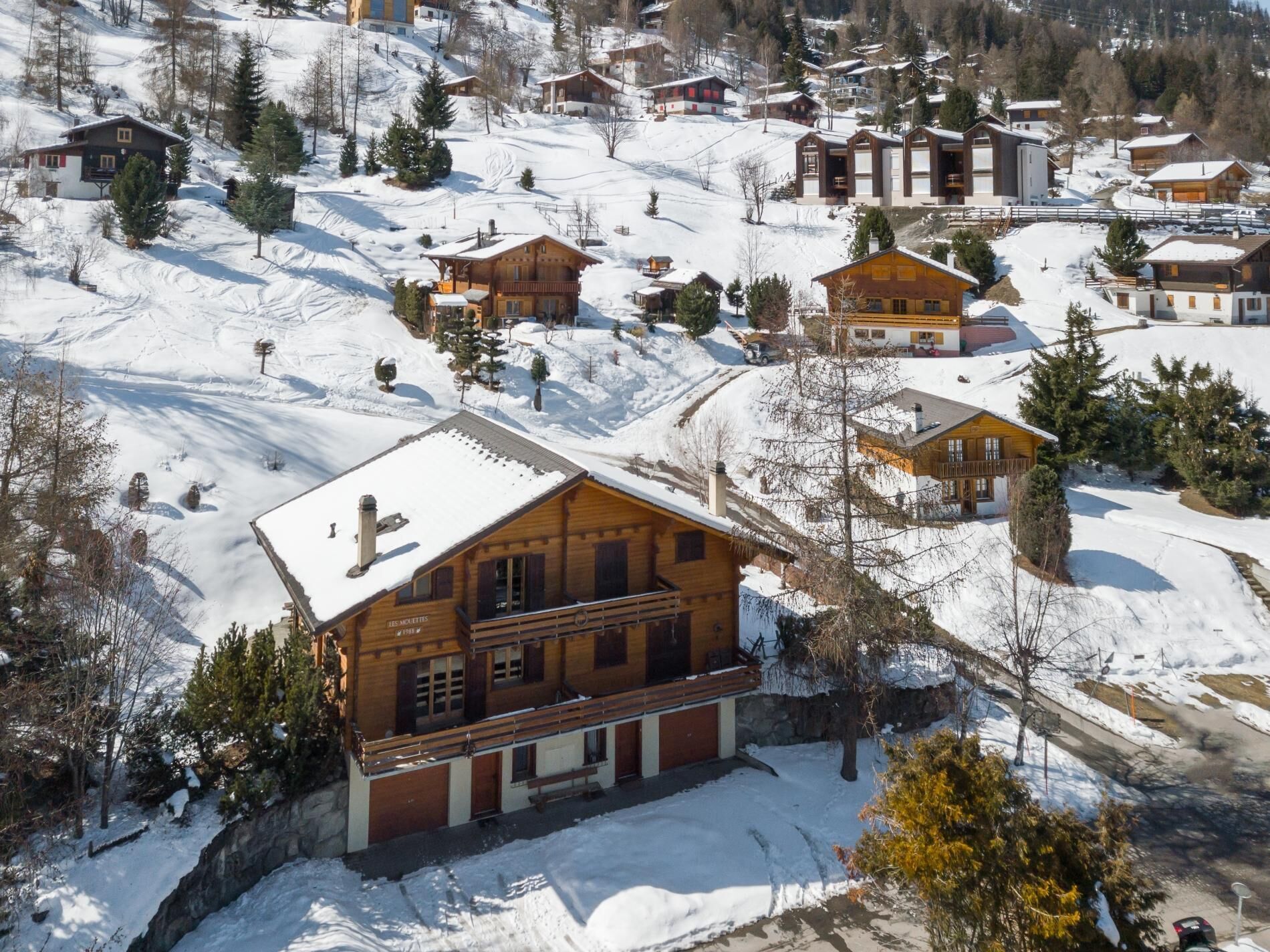 A snow-covered mountain village with wooden houses and a prominent lodge with a balcony.