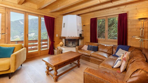 A wooden cabin interior with a sofa, a table, and a fireplace. - Chalet Mouettes (Riddes)