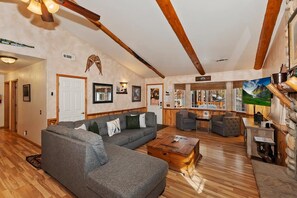 A spacious living room with a large sectional sofa, a wooden coffee table, and a stone fireplace.