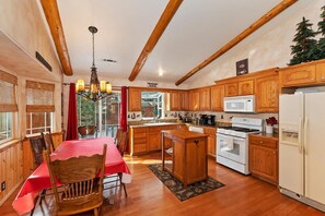 A kitchen with wooden cabinets, a dining table with chairs, a chandelier, and a view of the outdoors.