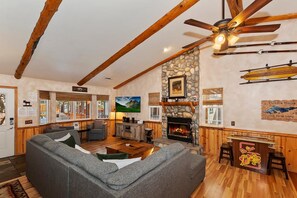 A cozy living room with a stone fireplace, wooden beams, and a large window.