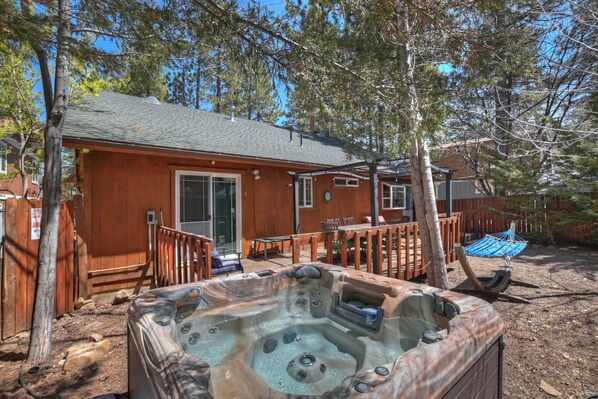 Una cabaña de madera con jacuzzi, terraza y patio trasero cercado.