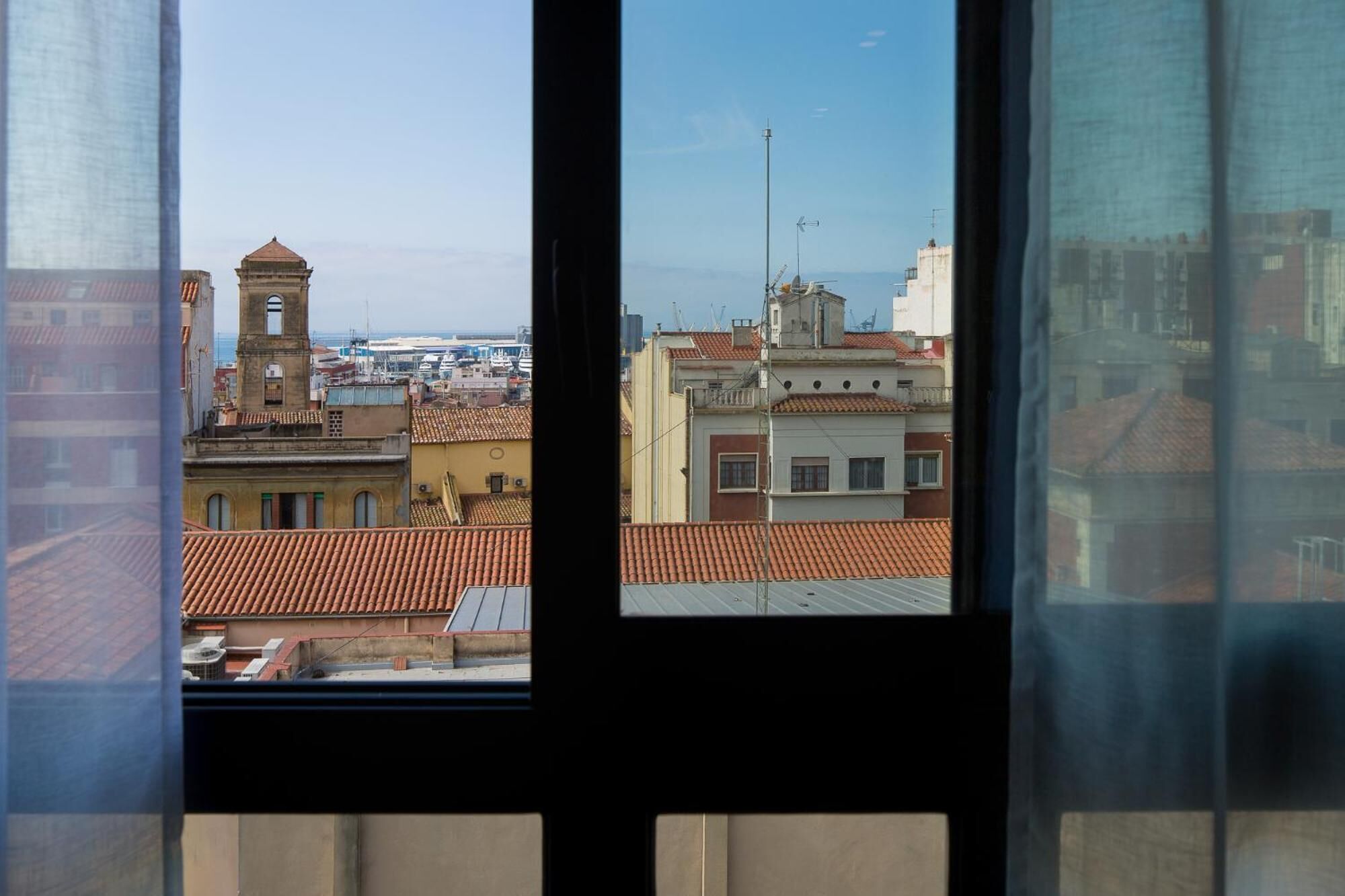 Visão pela janela de um horizonte urbano com edifícios, uma torre e um calhavele.