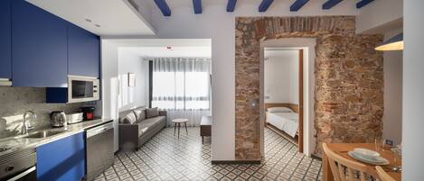 A modern hotel room with a kitchenette, a sofa, a small table, and a stone accent wall.