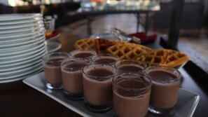 A table with a waffle, several glasses of chocolate drink, and stacked plates. - Grand Victoria Hotel (Samarinda)