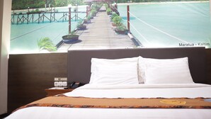 A hotel room with a bed, a nightstand with a phone and a lamp, and a poster of a beach scene. - Grand Victoria Hotel (Samarinda)