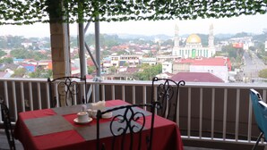 A balcony with a table set for dining, overlooking a cityscape with a prominent building with a golden dome. - Grand Victoria Hotel (Samarinda)
