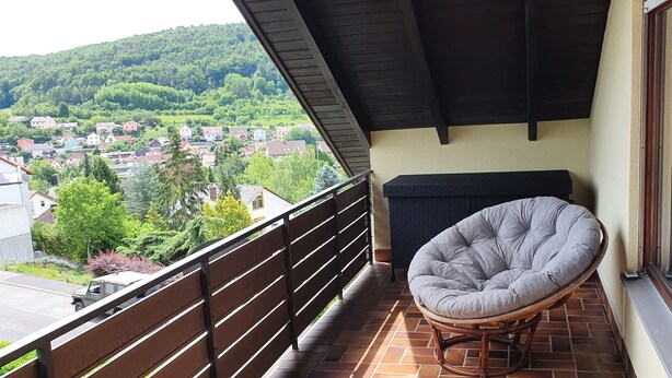A balcony with a wicker chair, a view of a town, and a tiled floor. - Gepflegte Dachgeschosswohnung im 2-familienhaus in Ruhiger Wohnlage (Bad Kissingen)