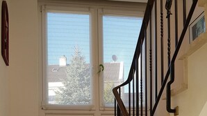 A staircase with a wooden handrail and black balusters, leading to a landing with windows and a view of the outside. - Gepflegte Dachgeschosswohnung im 2-familienhaus in Ruhiger Wohnlage (Bad Kissingen)