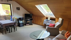 A cozy attic room with a dining table, a sofa, a TV, and a skylight. - Gepflegte Dachgeschosswohnung im 2-familienhaus in Ruhiger Wohnlage (Bad Kissingen)