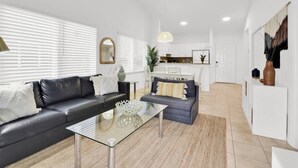 A modern living room with a black leather sofa, a glass coffee table, and a grey sofa. There is a kitchen area in the background with white cabinets and a dining table. - 350D - Boca Retreat w/ Pool, Parking, Near Evert Tennis & Shops (Boca Raton)