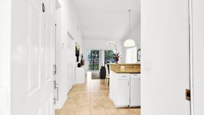 A bright, white interior with a kitchen area featuring a granite countertop, a hanging pendant light, and a view of the outdoors. - 350D - Boca Retreat w/ Pool, Parking, Near Evert Tennis & Shops (Boca Raton)
